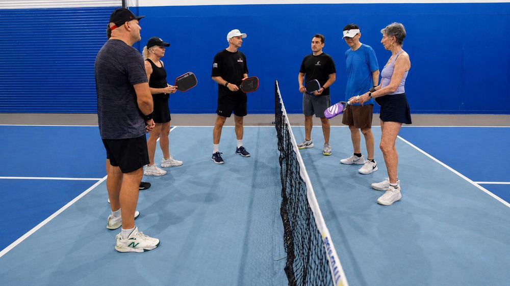 A Breakthrough coach demonstrating a shot to a group of players at the net on an indoor court